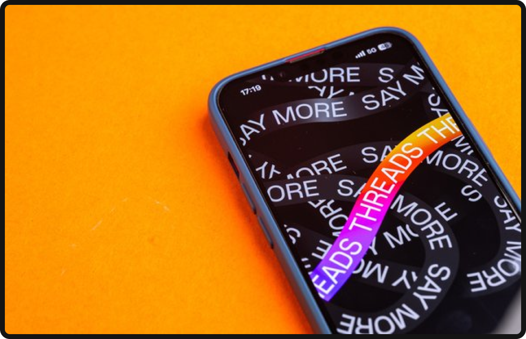 Phone on an orange background with the Threads app opening.